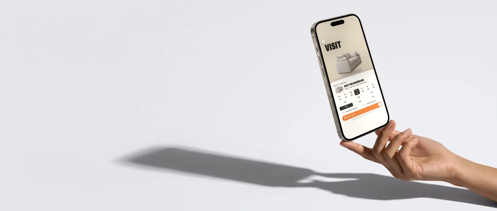 A phone balanced on fingertips showing the last step of a playable campaign: book a showroom visit