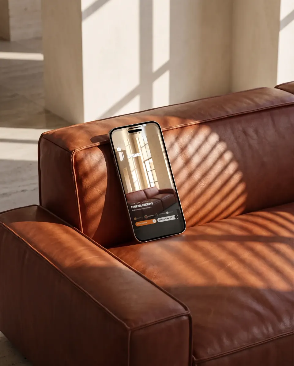 A phone resting on a cognac leather sofa in striped sunlight, showing that sofa's colours in a shoppable video